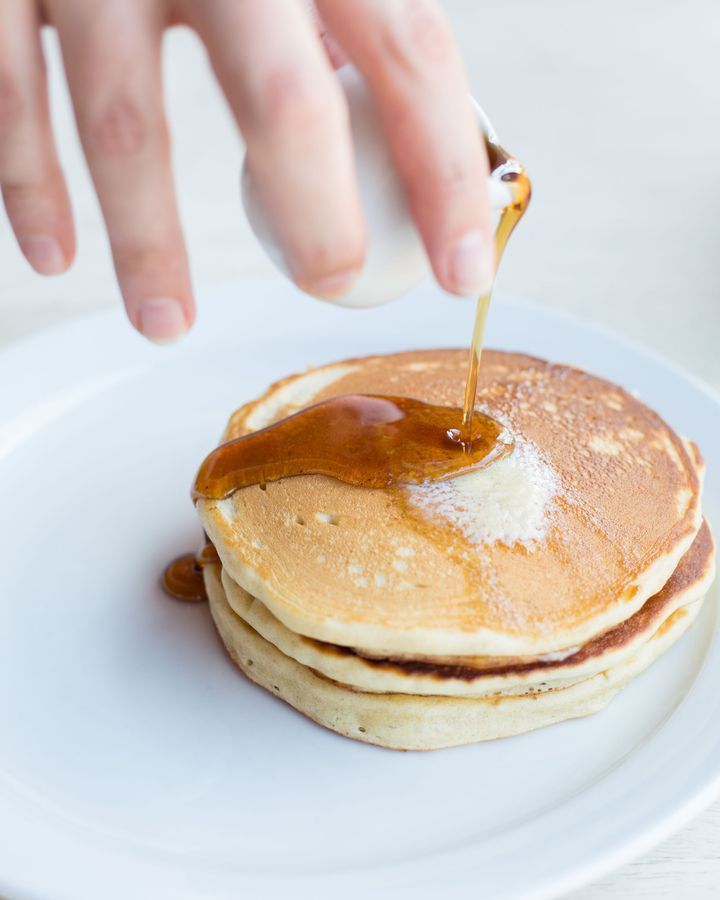 Stack of American-style pancakes with melted butter and maple syrup pouring over