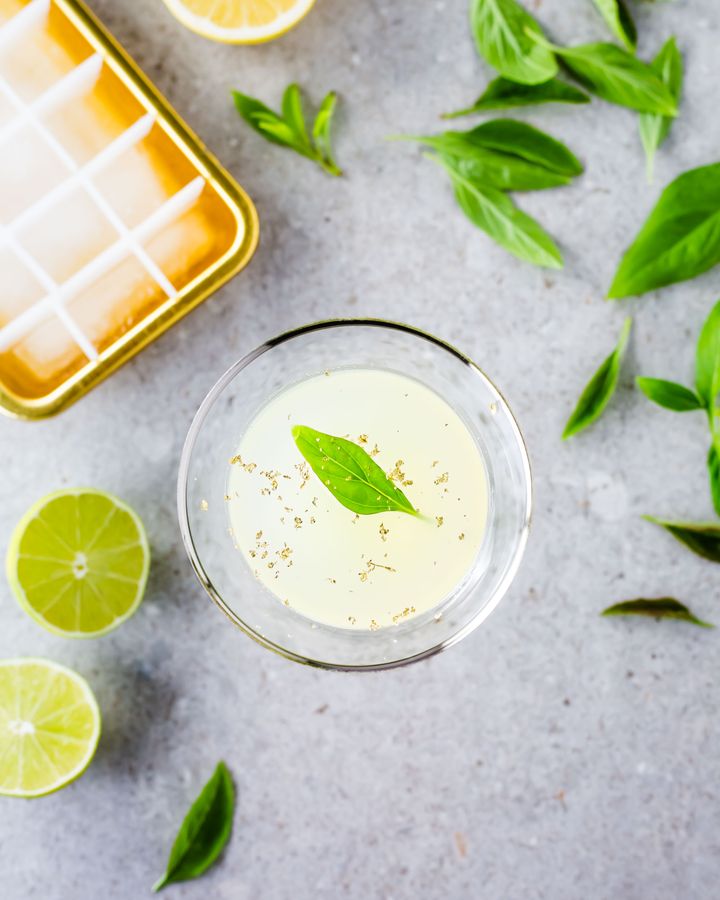 Margarita cocktail with Thai basil, surrounded by lime halves and Thai basil leaves