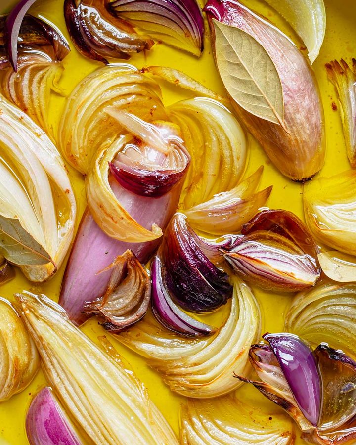 Close up of confit shallots and red onion with olive oil and bay leaves