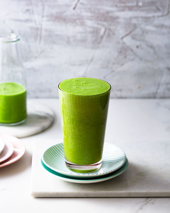 Glass of bright green smoothie on a white background with a bottle of green smoothie on the left