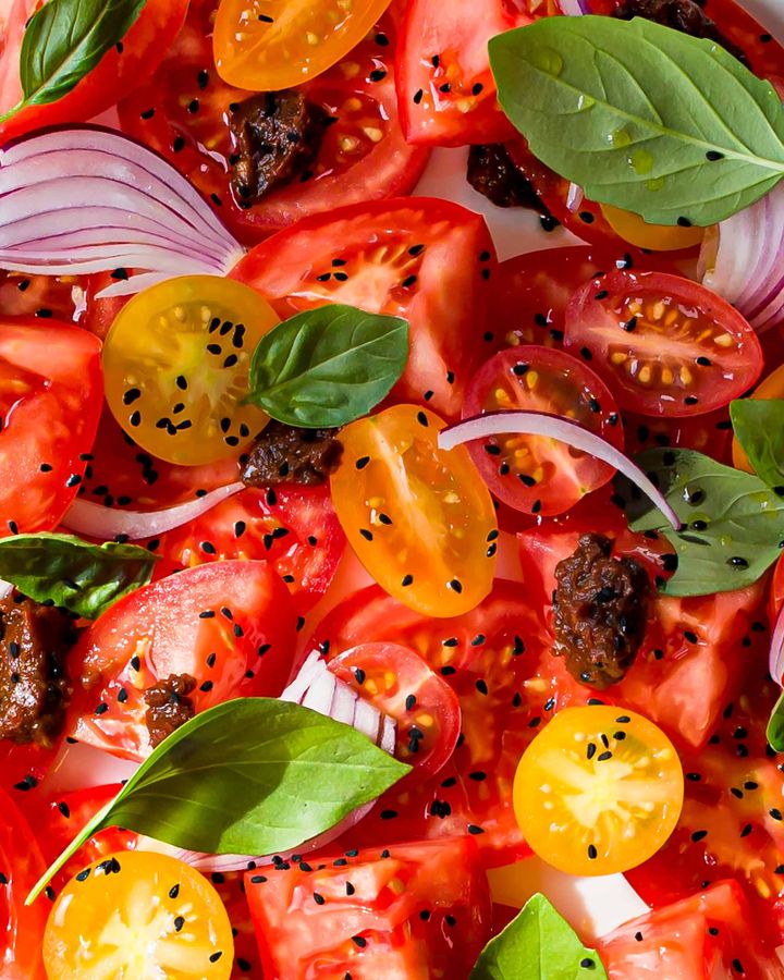 Close up of tomato salad with sun-dried tomato pesto, basil leaves and nigella seeds