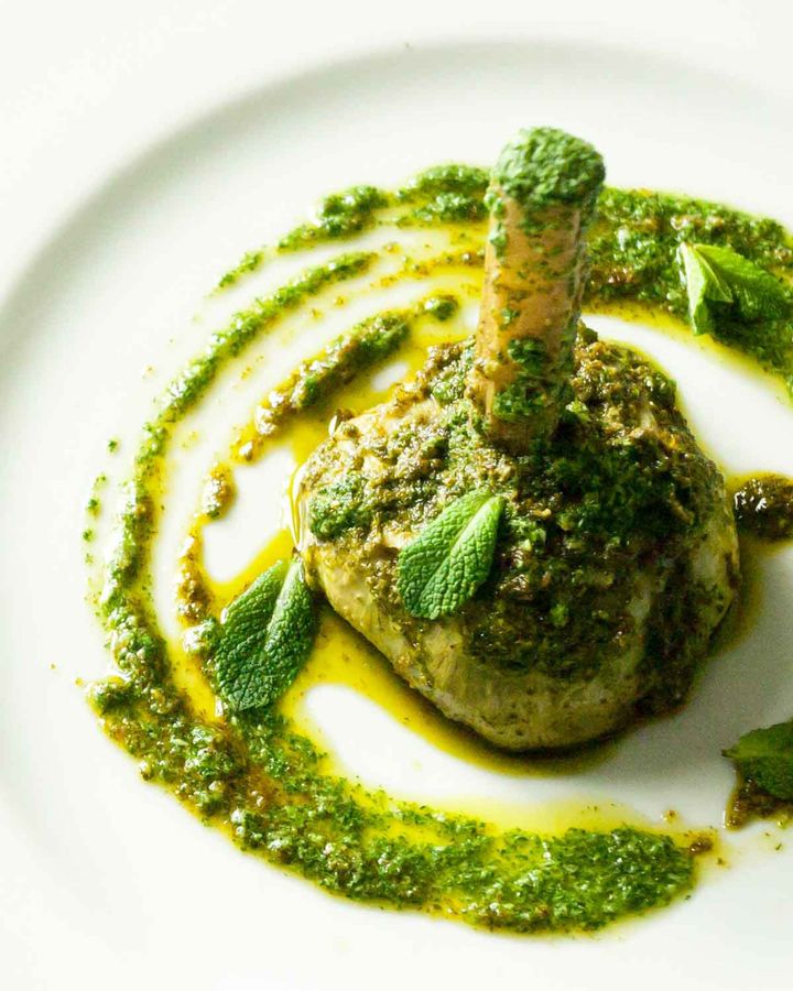 Braised whole artichoke with mint pesto on a white plate